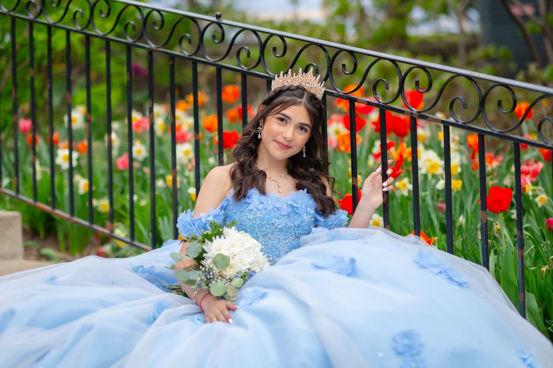 Quinceañera in a blue floral gown and crown holding a bouquet in a poppy field at Lilacia Park, Lombard, IL